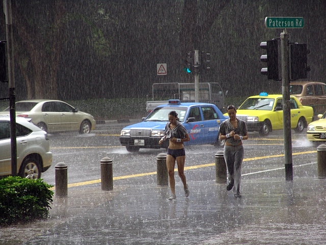 Two similar women in the rain with taxis behind them.